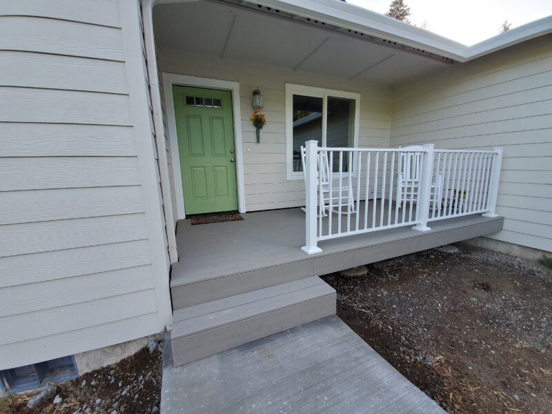 Gray composite front porch deck with steps and white aluminum picket railing beside a green front door
