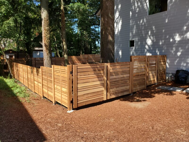 Horizontal-board cedar privacy fence with matching gate wrapping a corner backyard