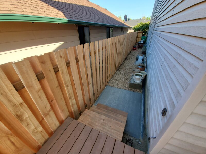 Cedar shadowbox fence along a narrow side yard with new concrete pathway and deck boards.