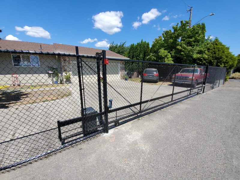 Black chain-link fence with a long rolling driveway gate in front of a residential property.