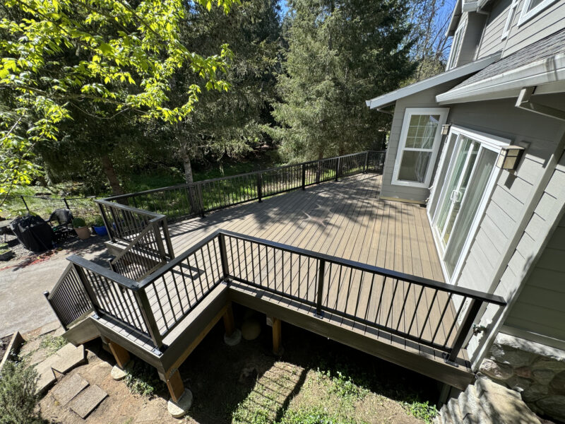 Large composite deck with black aluminum baluster railing and staircase overlooking a wooded backyard