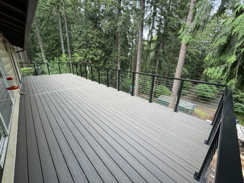 Spacious gray composite deck with black cable railing overlooking a forested backyard