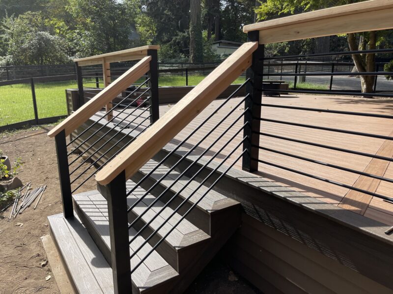 Composite deck stairs with black horizontal-rod railing and cedar handrail cap in warm afternoon sun
