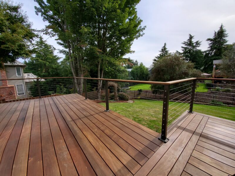 Expansive ipe hardwood deck with stainless cable railing overlooking a green backyard lawn