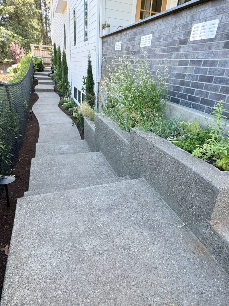 Exposed-aggregate concrete steps and walkway with a terraced concrete planter wall and fresh landscaping