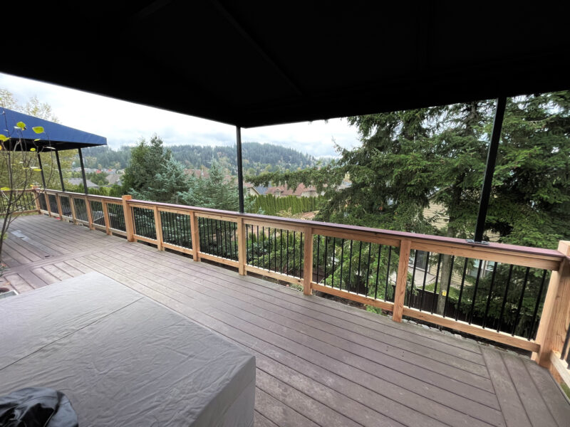 Covered composite deck with cedar and black metal baluster railing overlooking a wooded valley.