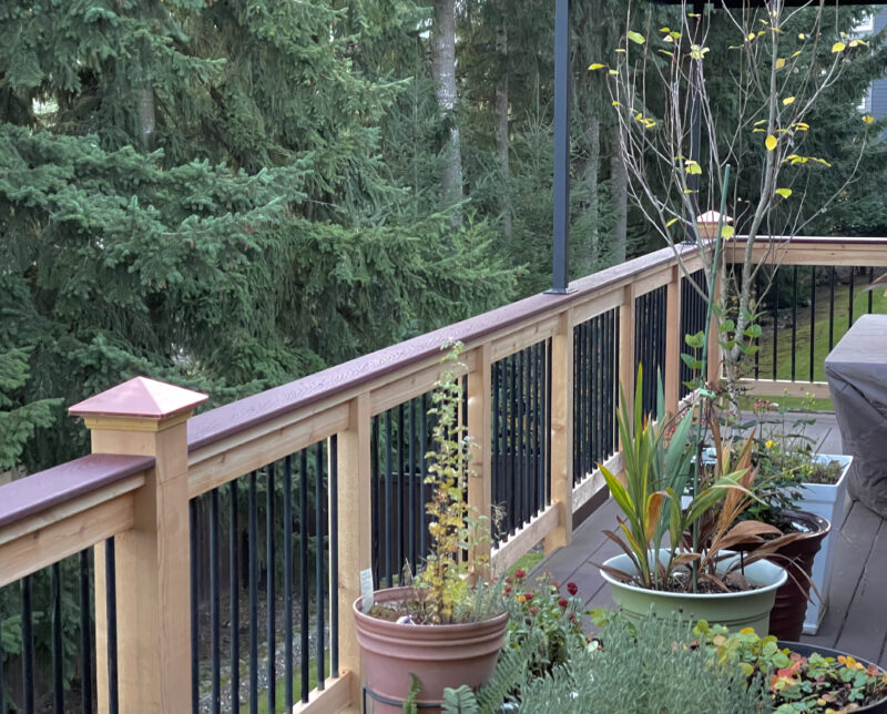 Close-up of cedar deck railing with black aluminum balusters, composite top cap, and copper post caps
