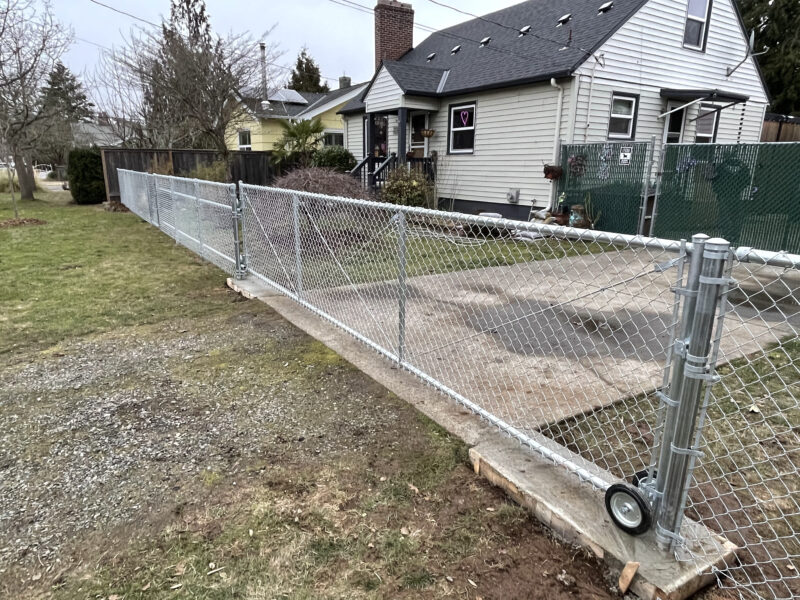 Galvanized chain-link fence with rolling gate on a new concrete curb along a residential driveway.